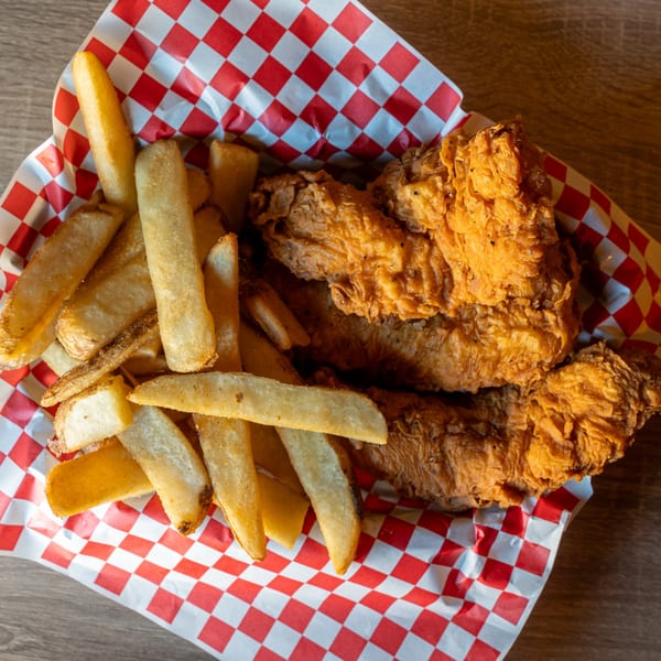 Crispy fried chicken tenders and thick-cut fries in a red and white checkered paper basket.