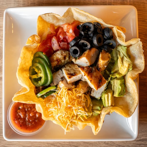Chicken taco salad in a crispy tortilla bowl with salsa, avocado, olives, and jalapenos.