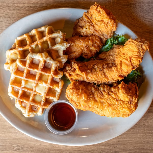 Crispy fried chicken tenders and waffles with syrup and lettuce on a white plate.